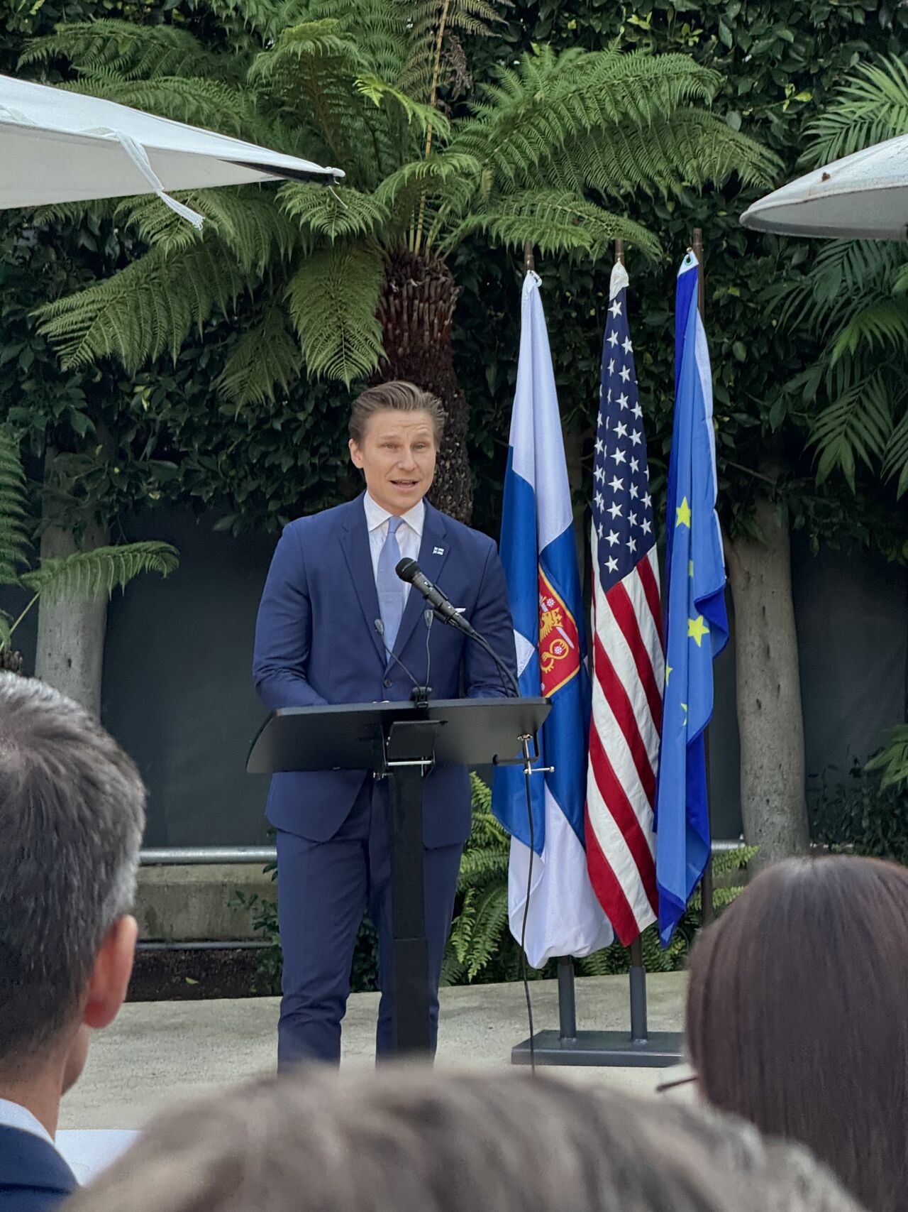 Minister of Defence Antti Häkkänen addresses attendees at Finland's Independence Day reception in Los Angeles, with Finnish, US, and EU flags displayed.